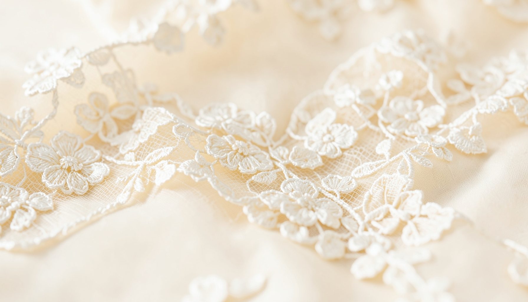 Elegant close-up of ivory lace fabric with delicate floral embroidery, softly lit against a cream background, refined mood