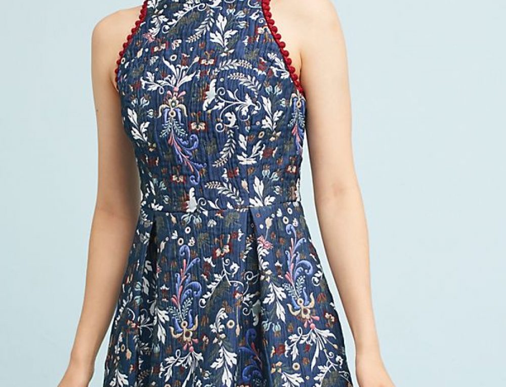 Cropped torso view of a person wearing a navy floral jacquard sleeveless dress with red trim against a plain light backdrop