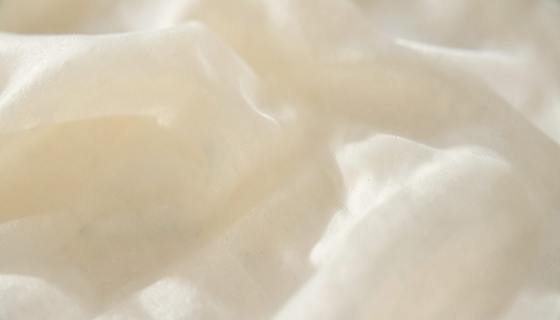 Soft, draped cream-colored fabric with gentle folds and subtle light, calm neutral mood